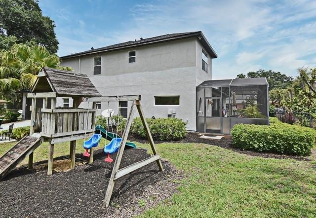 rear view of property with a playground, a yard, stucco siding, and a lanai