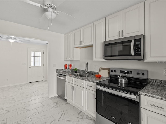 kitchen featuring stainless steel appliances, a sink, ceiling fan, light marble finish floors, and baseboards