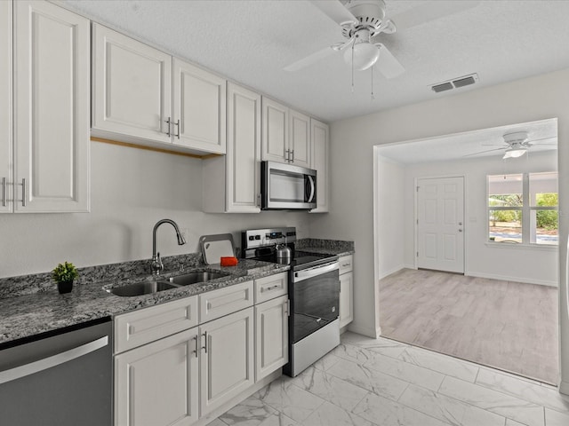 kitchen with stainless steel appliances, a sink, a ceiling fan, and light marble finish floors