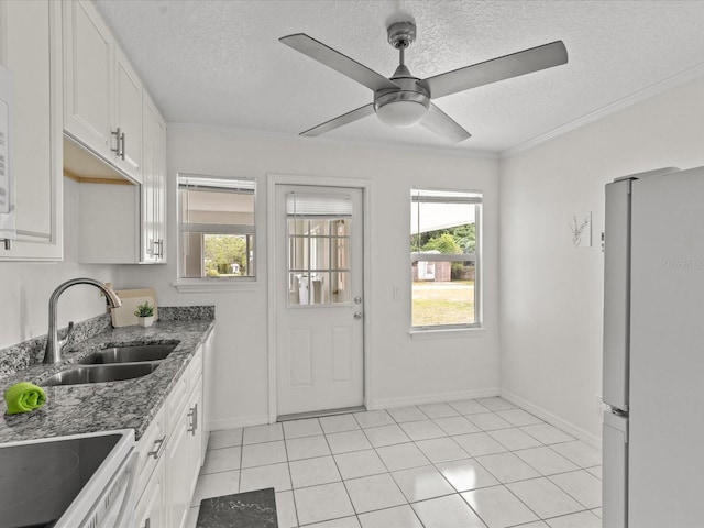 kitchen with freestanding refrigerator, a sink, a textured ceiling, ceiling fan, and baseboards