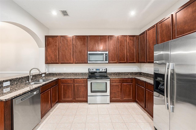 kitchen featuring stainless steel appliances, a sink, dark stone counters, a peninsula, and arched walkways