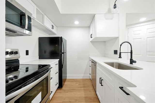 kitchen featuring stainless steel appliances, a sink, baseboards, light wood-style flooring, and light countertops