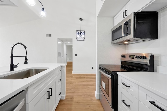 kitchen featuring appliances with stainless steel finishes, a sink, lofted ceiling, light wood-style flooring, and white cabinets
