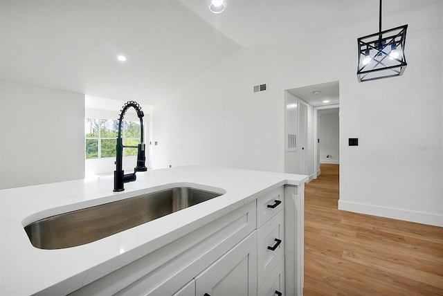 kitchen featuring a sink, vaulted ceiling, light wood-style floors, light countertops, and pendant lighting