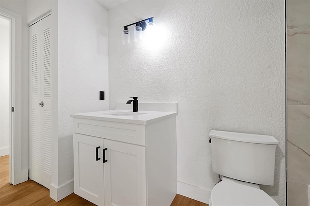 bathroom featuring a closet, wood finished floors, vanity, toilet, and a textured wall