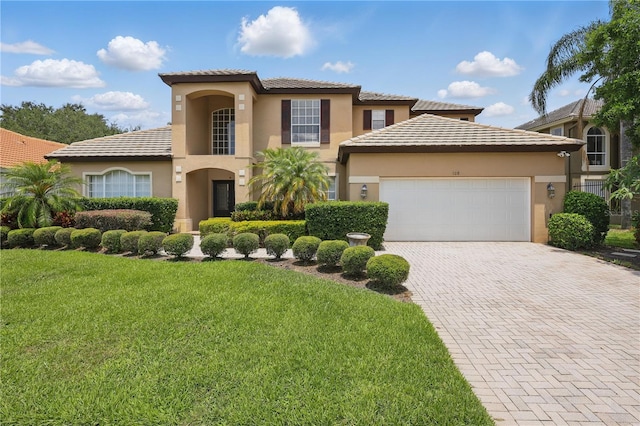 mediterranean / spanish-style house with stucco siding, an attached garage, a front yard, and decorative driveway