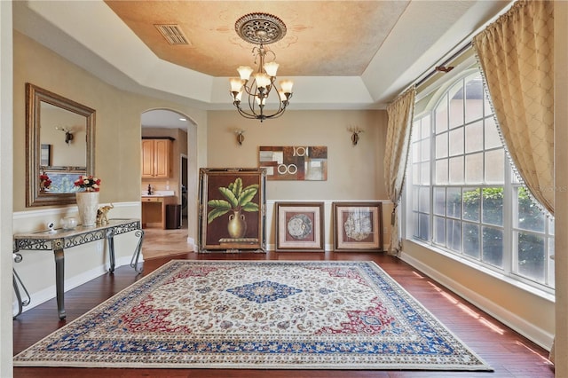 foyer featuring a chandelier, arched walkways, a tray ceiling, dark wood-type flooring, and baseboards