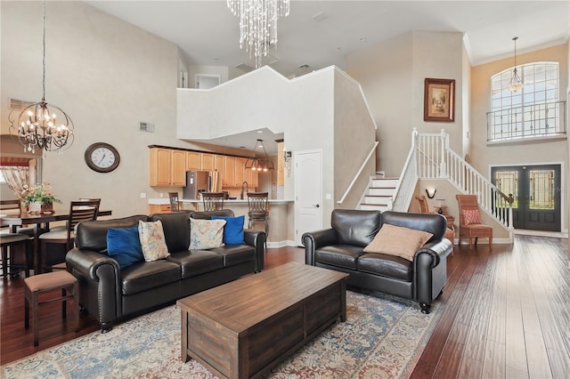 living area featuring a chandelier, a towering ceiling, stairs, wood-type flooring, and baseboards