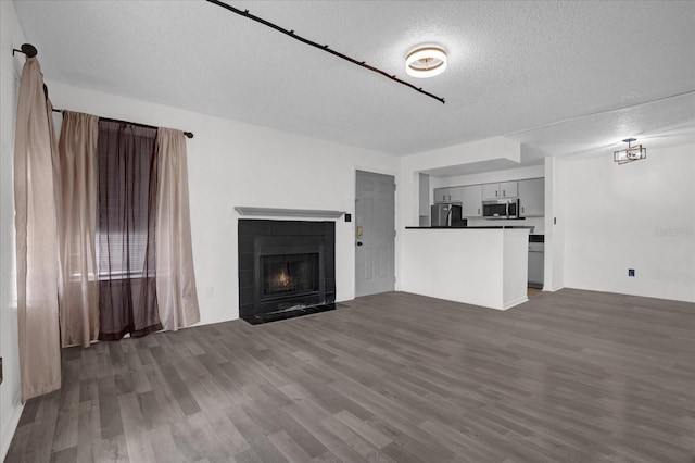 unfurnished living room with a textured ceiling, dark wood finished floors, and a tiled fireplace