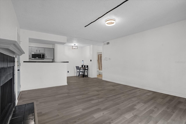 unfurnished living room with a tiled fireplace, a textured ceiling, and dark wood-type flooring