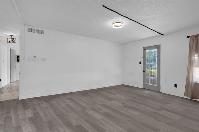 unfurnished room with a textured ceiling, wood finished floors, and baseboards