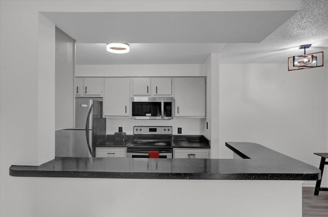 kitchen featuring appliances with stainless steel finishes, dark countertops, a textured ceiling, wood finished floors, and white cabinets