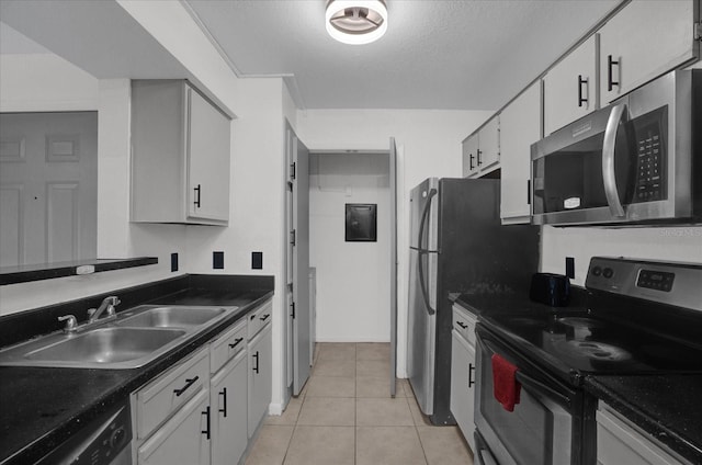kitchen with appliances with stainless steel finishes, a sink, dark countertops, light tile patterned floors, and white cabinets