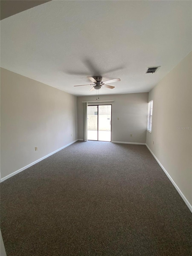empty room featuring ceiling fan, dark carpet, and plenty of natural light