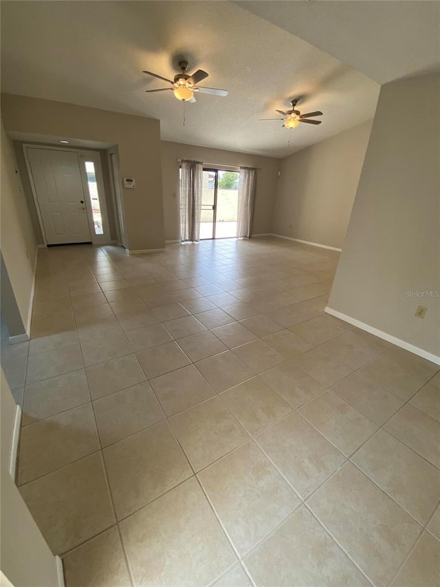 empty room featuring light tile patterned floors, a ceiling fan, and baseboards