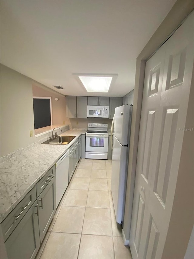 kitchen with white appliances, gray cabinetry, a sink, light countertops, and light tile patterned flooring