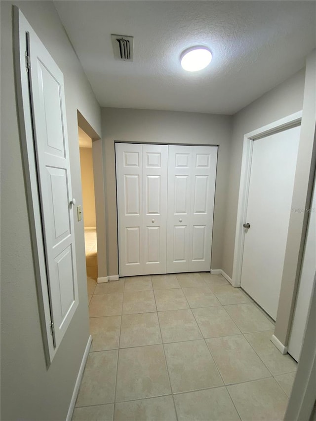 hall with baseboards, a textured ceiling, and light tile patterned floors