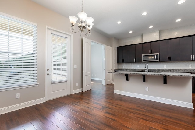 625 Pavia Loop, Lake Mary, FL 32746 - kitchen with stainless steel microwave, a breakfast bar area, a chandelier, dark wood-type flooring, and light stone counters