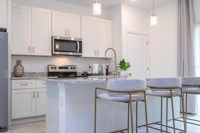 kitchen with appliances with stainless steel finishes, a kitchen island with sink, white cabinets, light stone countertops, and hanging light fixtures