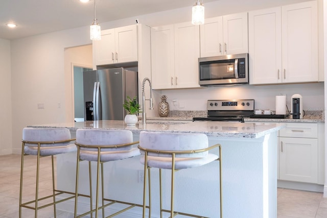 kitchen featuring stainless steel appliances, an island with sink, white cabinets, light tile patterned floors, and a breakfast bar
