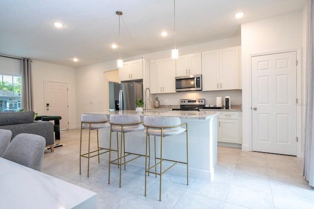 kitchen featuring appliances with stainless steel finishes, a kitchen island with sink, a breakfast bar, white cabinetry, and light stone countertops