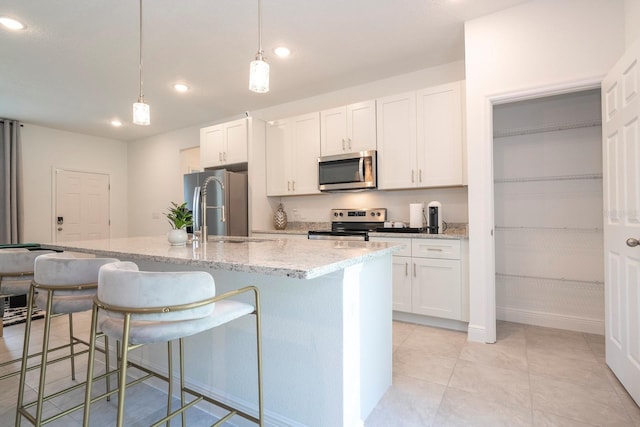 kitchen featuring stainless steel appliances, a sink, an island with sink, a breakfast bar, and white cabinets