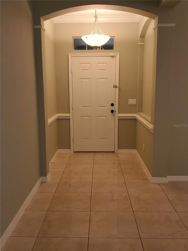 doorway to outside featuring arched walkways, crown molding, light tile patterned flooring, and baseboards
