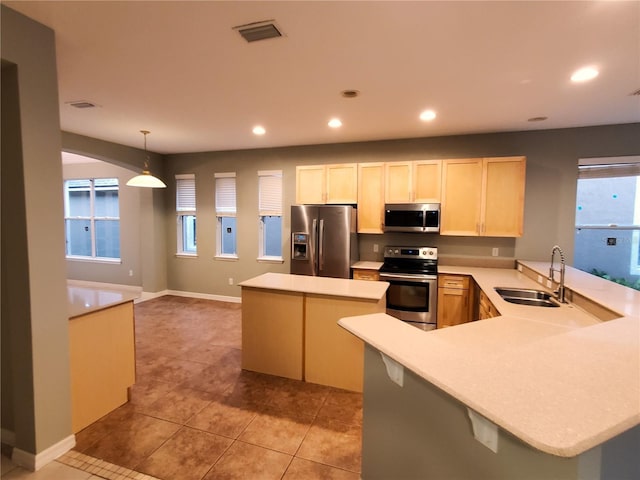 kitchen featuring appliances with stainless steel finishes, a sink, a kitchen island, light countertops, and light brown cabinets