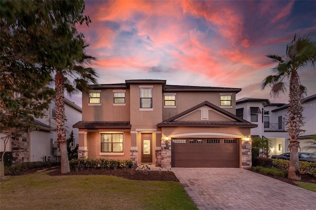 view of front of house with stucco siding, decorative driveway, stone siding, and a lawn