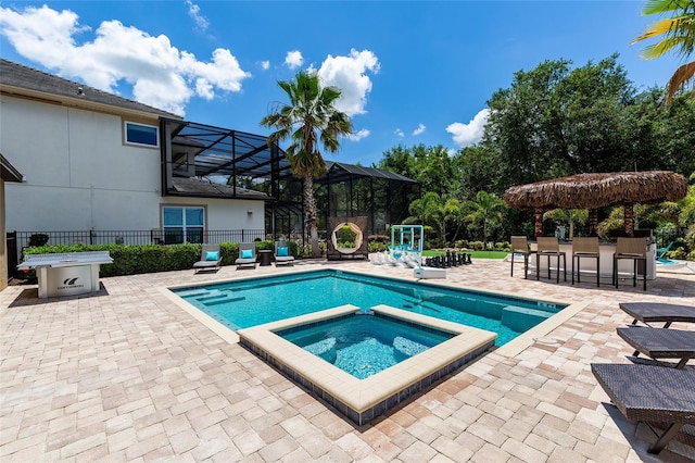 view of swimming pool with a patio, a pool with connected hot tub, fence, and glass enclosure