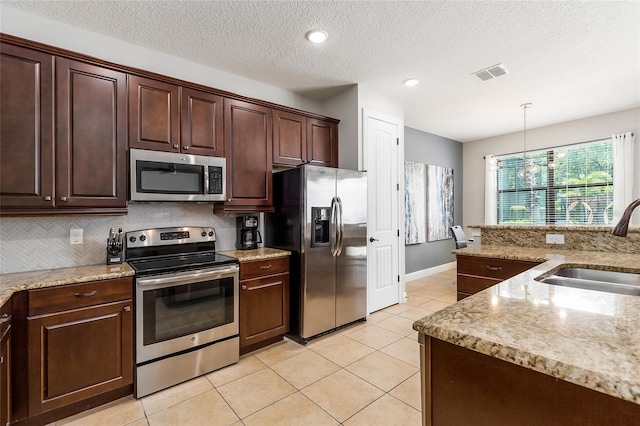 kitchen featuring appliances with stainless steel finishes, a sink, light tile patterned floors, backsplash, and dark brown cabinets