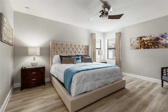bedroom with light wood-type flooring, ceiling fan, baseboards, and a textured ceiling