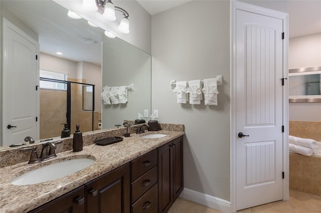 bathroom with a shower stall, double vanity, tile patterned flooring, and baseboards