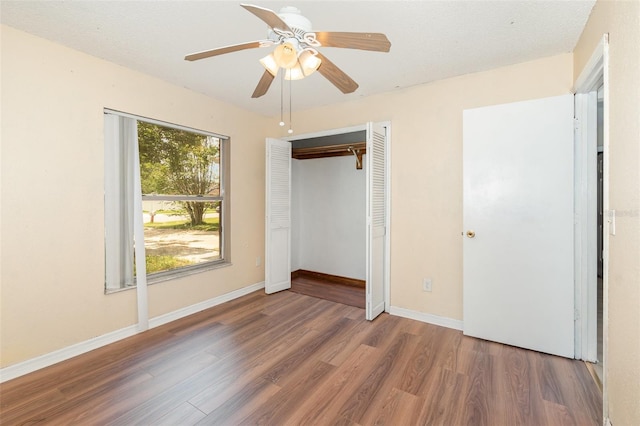 unfurnished bedroom with wood finished floors, a closet, baseboards, and a ceiling fan