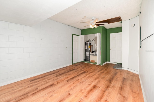 spare room featuring electric water heater, a ceiling fan, wood finished floors, and baseboards