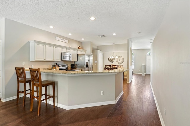 kitchen with appliances with stainless steel finishes, dark wood-type flooring, a peninsula, baseboards, and a textured ceiling