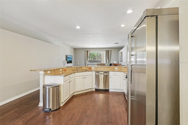 kitchen with stainless steel appliances, dark wood-style floors, a sink, a peninsula, and light stone counters