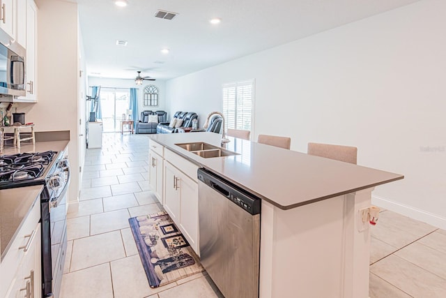 kitchen with appliances with stainless steel finishes, a sink, ceiling fan, a center island with sink, and light tile patterned floors