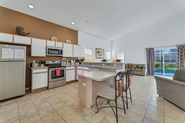 kitchen with appliances with stainless steel finishes, open floor plan, high vaulted ceiling, a peninsula, and white cabinetry
