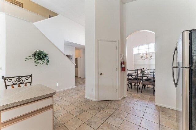 entryway featuring baseboards, a chandelier, light tile patterned floors, a high ceiling, and stairs