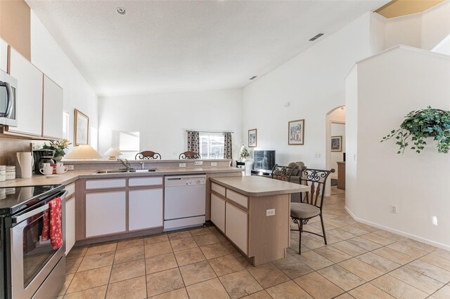 kitchen featuring appliances with stainless steel finishes, a sink, arched walkways, a peninsula, and plenty of natural light