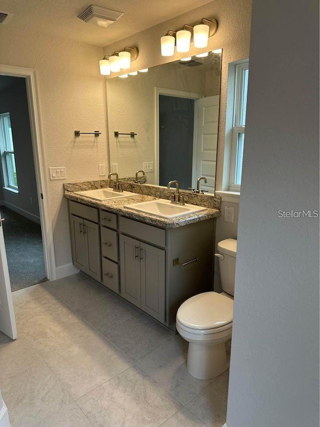 bathroom with tile patterned flooring, a textured wall, toilet, and double vanity