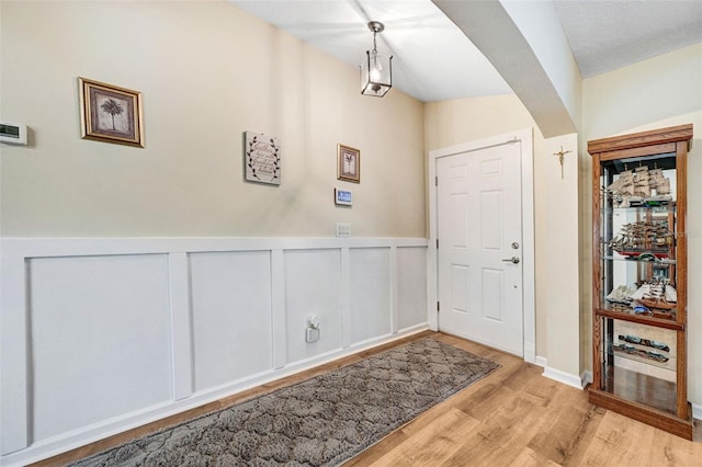 entryway with wood finished floors and a wainscoted wall