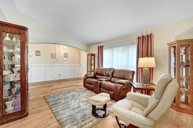 living room featuring arched walkways, vaulted ceiling, light wood finished floors, a wainscoted wall, and decorative columns