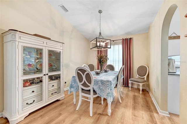 dining area with a chandelier, arched walkways, light wood finished floors, baseboards, and lofted ceiling
