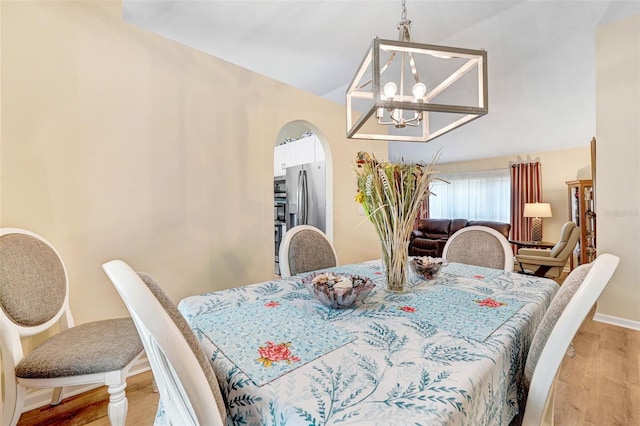 dining area featuring light wood-type flooring, arched walkways, vaulted ceiling, a chandelier, and baseboards