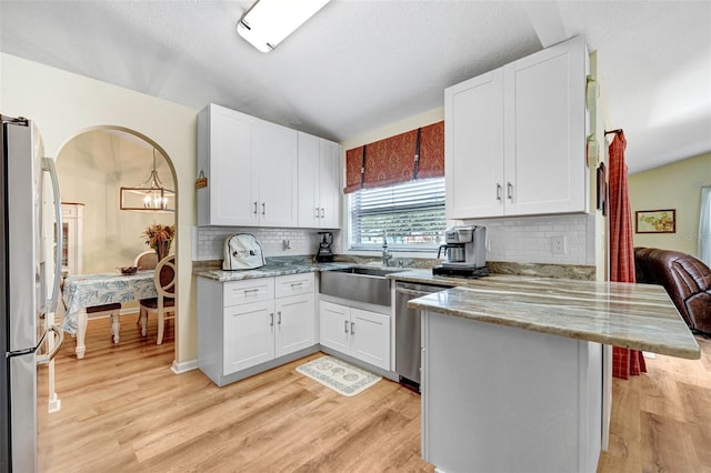 kitchen featuring stainless steel appliances, a sink, a peninsula, light wood-type flooring, and vaulted ceiling