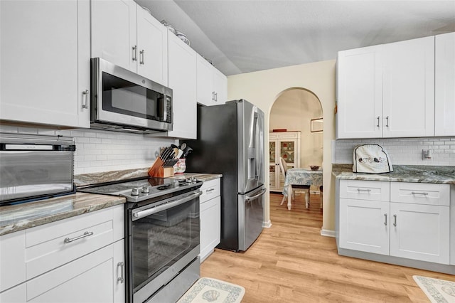 kitchen with appliances with stainless steel finishes, arched walkways, light wood-style flooring, decorative backsplash, and light stone counters