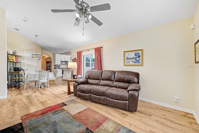 living room with arched walkways, light wood-style floors, ceiling fan, vaulted ceiling, and baseboards