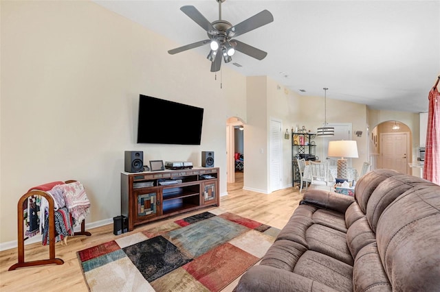 living room featuring arched walkways, ceiling fan, baseboards, wood finished floors, and a high ceiling